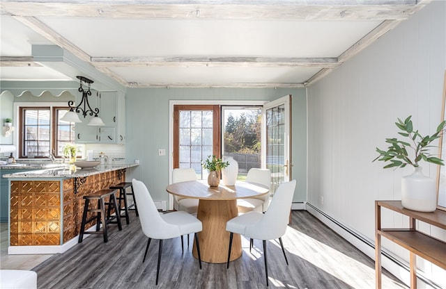 dining area featuring beamed ceiling, a baseboard heating unit, dark wood-type flooring, and wood walls