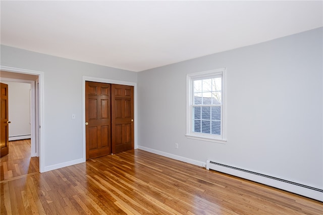 unfurnished bedroom with light wood-type flooring, a baseboard radiator, and a closet