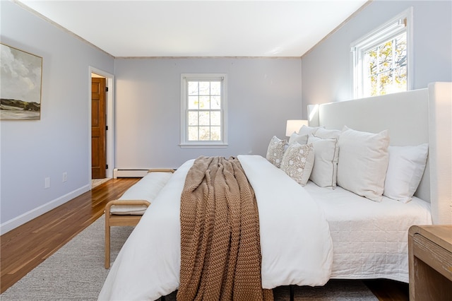 bedroom featuring multiple windows, hardwood / wood-style floors, a baseboard heating unit, and ornamental molding