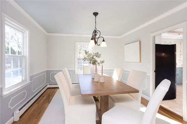 dining area featuring a chandelier, ornamental molding, wood-type flooring, and a baseboard heating unit