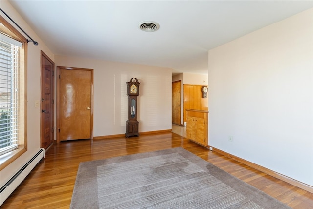 unfurnished room with wood-type flooring, a baseboard radiator, and a healthy amount of sunlight