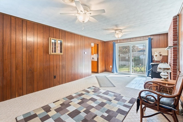 sitting room featuring ceiling fan, light colored carpet, and wooden walls