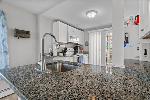 kitchen with dark stone countertops, white appliances, white cabinetry, and kitchen peninsula