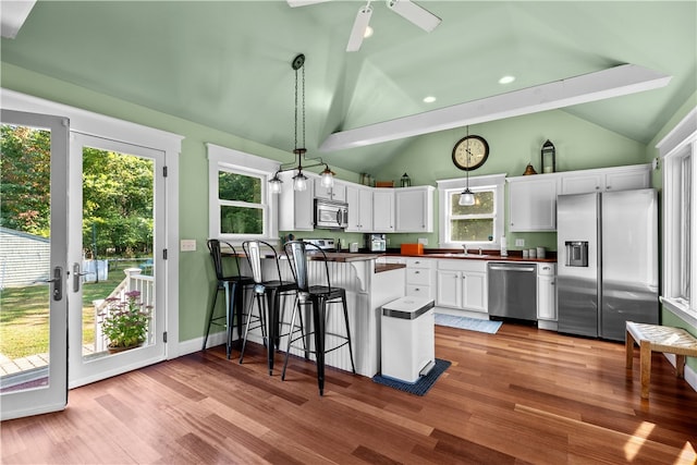 kitchen featuring appliances with stainless steel finishes, vaulted ceiling, white cabinetry, and hanging light fixtures