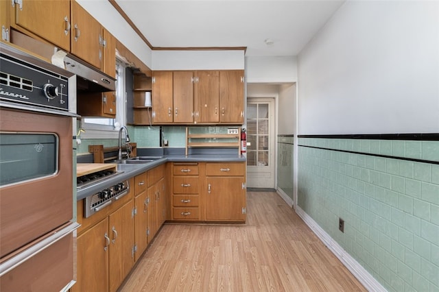 kitchen with light wood-type flooring, wall oven, sink, tile walls, and stainless steel gas stovetop