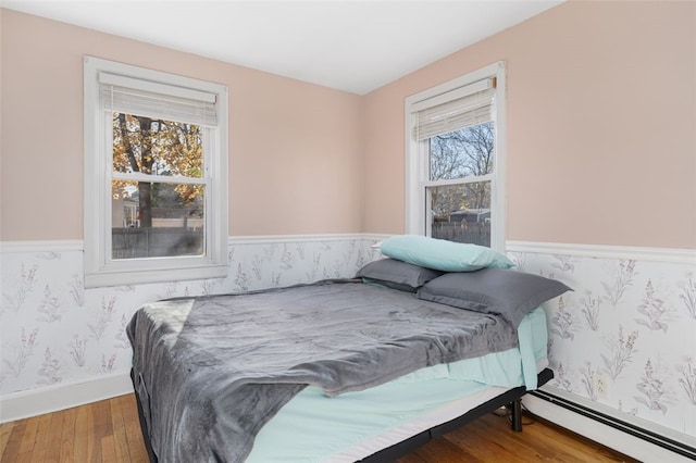 bedroom with multiple windows, hardwood / wood-style floors, and a baseboard heating unit