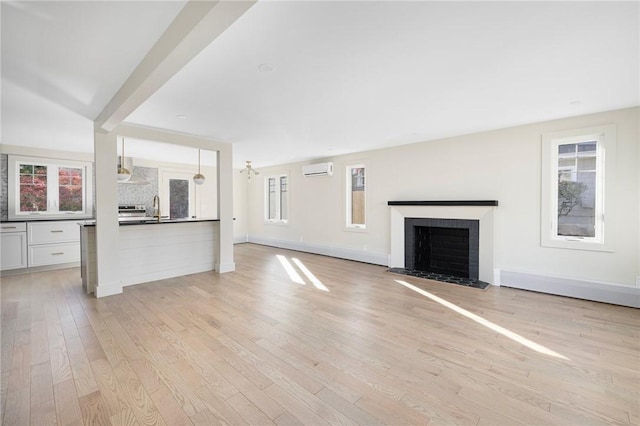 unfurnished living room with a brick fireplace, light hardwood / wood-style floors, a wall mounted air conditioner, and sink