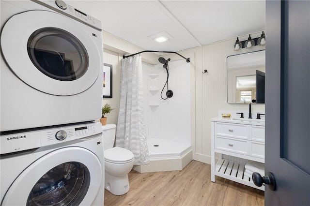 bathroom with hardwood / wood-style flooring, curtained shower, toilet, stacked washing maching and dryer, and vanity