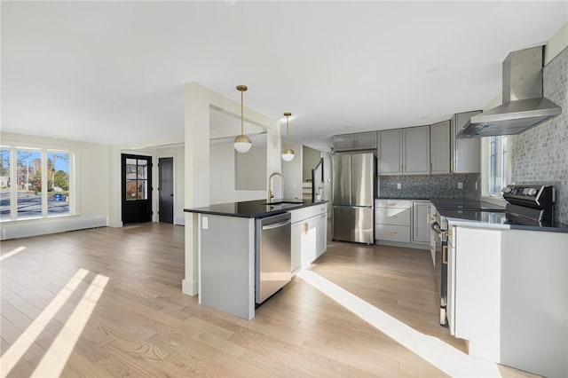 kitchen with light hardwood / wood-style flooring, tasteful backsplash, stainless steel appliances, wall chimney range hood, and decorative light fixtures