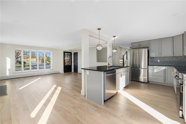 kitchen featuring hanging light fixtures, light wood-type flooring, stainless steel appliances, decorative backsplash, and sink