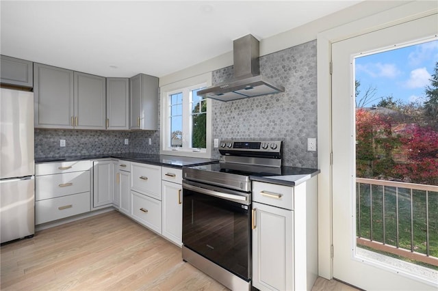 kitchen featuring light wood-type flooring, gray cabinetry, tasteful backsplash, appliances with stainless steel finishes, and wall chimney range hood