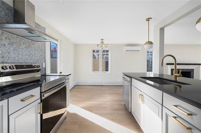 kitchen with decorative light fixtures, light hardwood / wood-style floors, sink, appliances with stainless steel finishes, and wall chimney exhaust hood