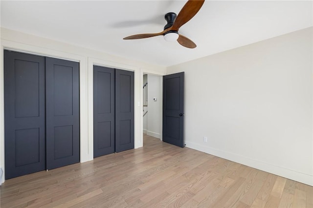 unfurnished bedroom featuring ceiling fan, light hardwood / wood-style flooring, and multiple closets