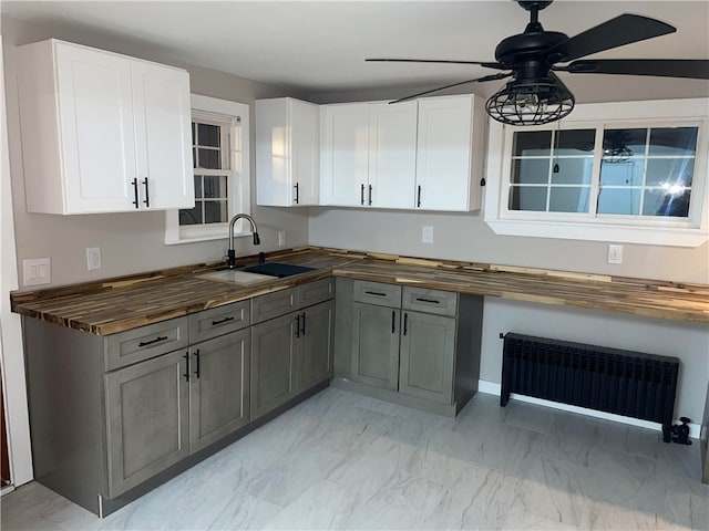 kitchen featuring wooden counters, radiator, ceiling fan, sink, and white cabinets