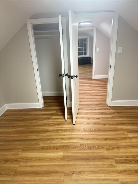 additional living space featuring light hardwood / wood-style floors, lofted ceiling, and radiator