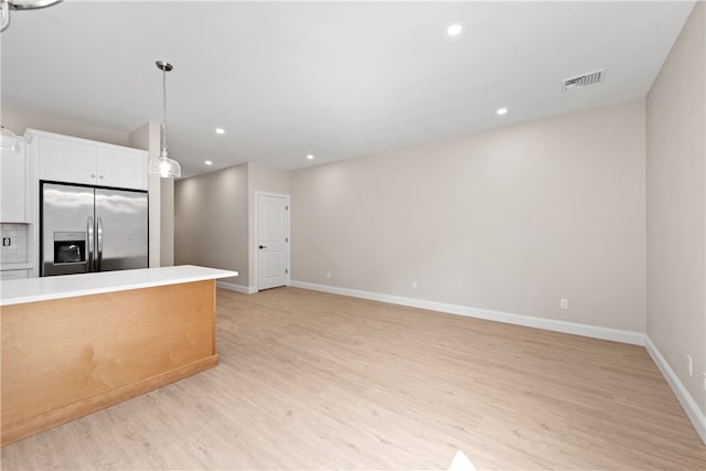 kitchen with white cabinetry, hanging light fixtures, tasteful backsplash, stainless steel fridge, and light hardwood / wood-style floors