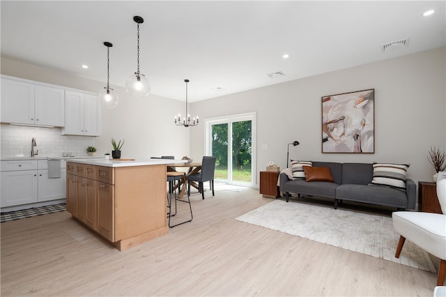 kitchen with light wood-type flooring, tasteful backsplash, decorative light fixtures, a center island, and white cabinetry