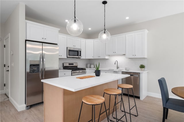 kitchen with light wood-type flooring, appliances with stainless steel finishes, tasteful backsplash, a kitchen island, and white cabinetry