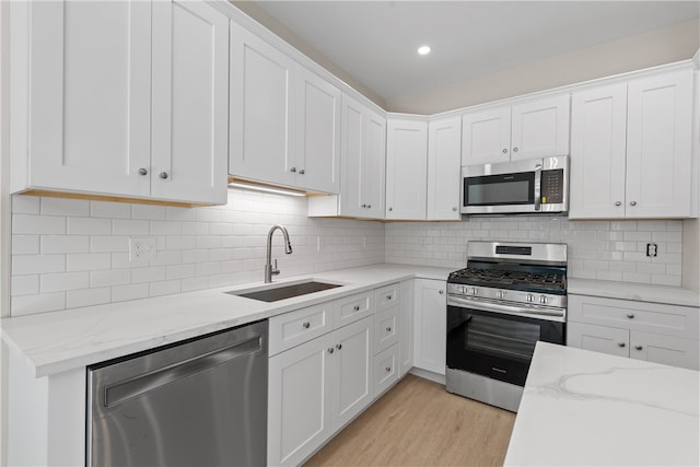 kitchen featuring white cabinets, sink, light wood-type flooring, tasteful backsplash, and stainless steel appliances