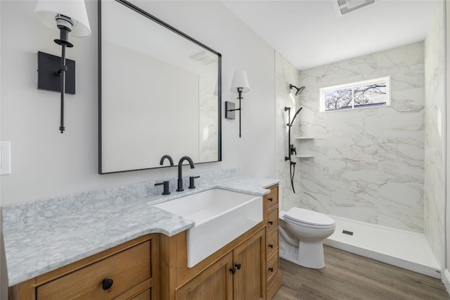 bathroom with hardwood / wood-style floors, vanity, toilet, and a tile shower