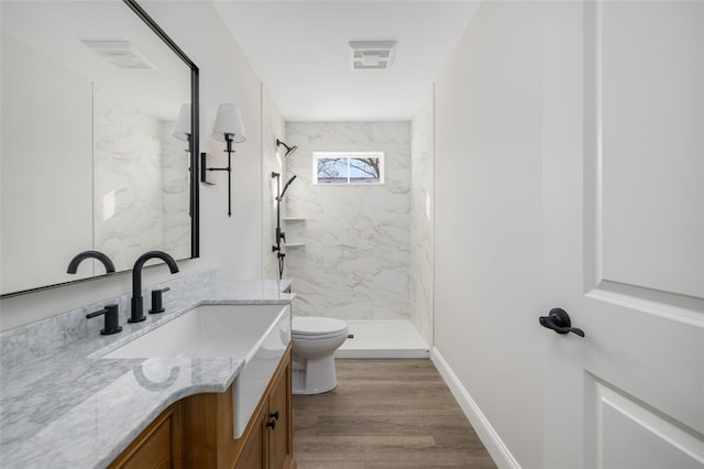 bathroom featuring a tile shower, vanity, wood-type flooring, and toilet