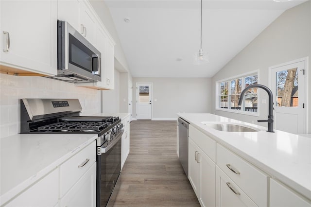 kitchen with appliances with stainless steel finishes, vaulted ceiling, pendant lighting, light hardwood / wood-style flooring, and white cabinets