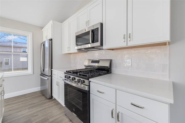 kitchen with backsplash, light wood-type flooring, appliances with stainless steel finishes, light stone counters, and white cabinetry