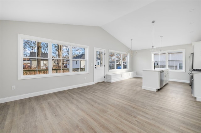 unfurnished living room with plenty of natural light, light hardwood / wood-style floors, sink, and vaulted ceiling