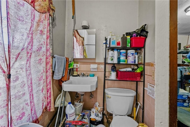 bathroom with toilet, tile walls, and sink