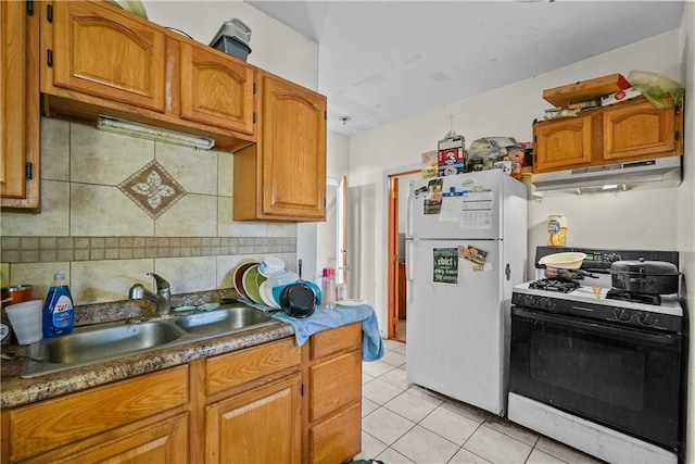 kitchen featuring sink, white fridge, gas range oven, light tile patterned flooring, and tasteful backsplash