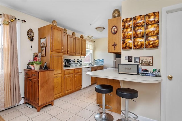 kitchen with a kitchen bar, light tile patterned floors, white dishwasher, and kitchen peninsula