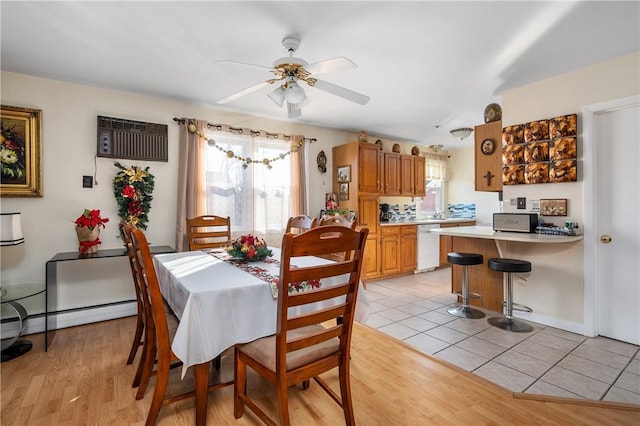 dining area with a wall mounted air conditioner, light hardwood / wood-style floors, a baseboard radiator, and ceiling fan