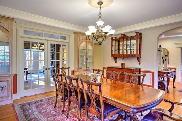 dining area with french doors, light hardwood / wood-style floors, an inviting chandelier, and ornamental molding