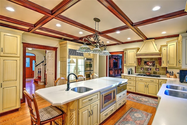 kitchen featuring a kitchen bar, custom range hood, built in appliances, decorative light fixtures, and light hardwood / wood-style floors