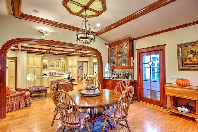 dining area featuring coffered ceiling, ornamental molding, indoor bar, and light hardwood / wood-style flooring