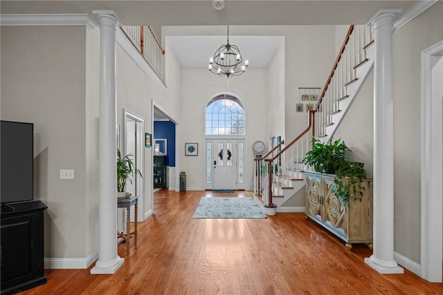 entryway featuring decorative columns, ornamental molding, a notable chandelier, and hardwood / wood-style flooring