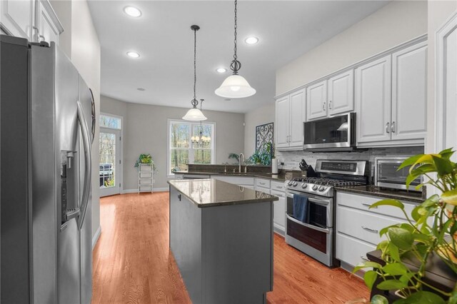 kitchen featuring white cabinets, hanging light fixtures, light wood-type flooring, appliances with stainless steel finishes, and a kitchen island