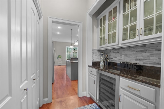 bar featuring white cabinetry, wine cooler, light hardwood / wood-style flooring, dark stone countertops, and decorative light fixtures