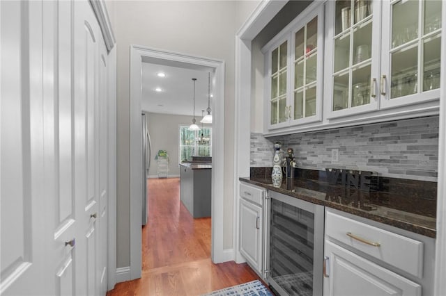 bar with light hardwood / wood-style flooring, tasteful backsplash, white cabinets, beverage cooler, and dark stone counters