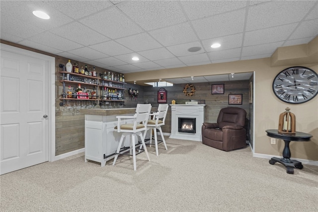 bar featuring a paneled ceiling, white cabinetry, light carpet, and wood walls