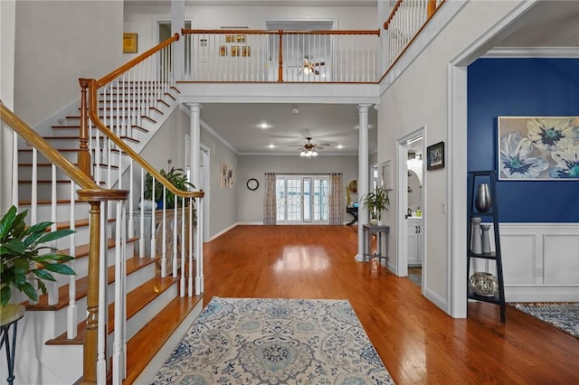 entryway featuring a ceiling fan, wood finished floors, crown molding, a towering ceiling, and ornate columns