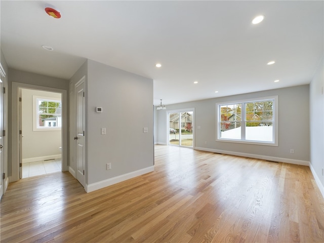 unfurnished living room with a notable chandelier, a healthy amount of sunlight, and light hardwood / wood-style floors