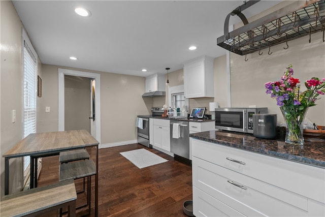 kitchen featuring stainless steel appliances, dark wood-type flooring, decorative light fixtures, dark stone countertops, and white cabinetry