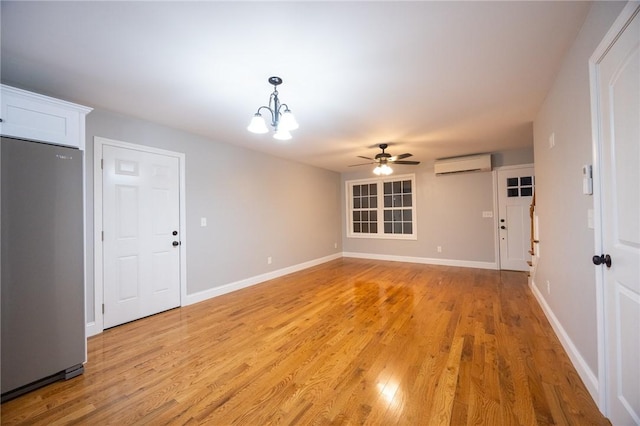 unfurnished living room featuring an AC wall unit, ceiling fan with notable chandelier, and light wood-type flooring