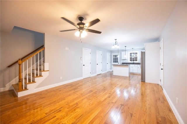 unfurnished living room featuring light hardwood / wood-style flooring and ceiling fan with notable chandelier