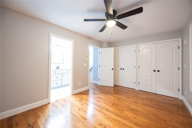 unfurnished bedroom with ensuite bathroom, light hardwood / wood-style flooring, ceiling fan, and multiple closets