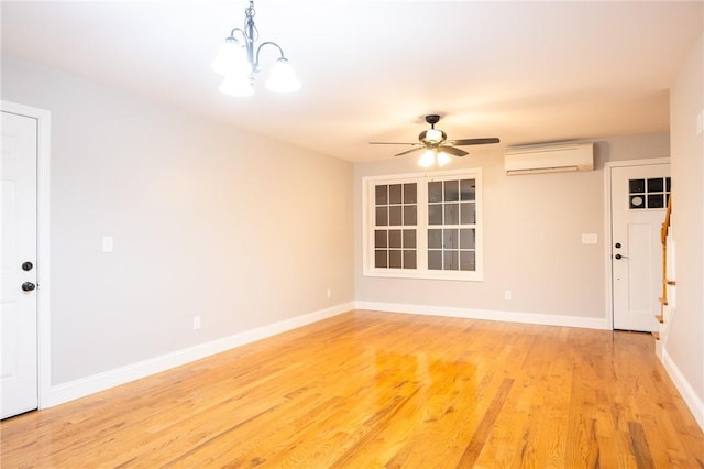 empty room featuring ceiling fan with notable chandelier, light hardwood / wood-style floors, and a wall mounted AC