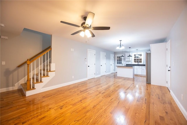 unfurnished living room featuring ceiling fan with notable chandelier and light hardwood / wood-style flooring