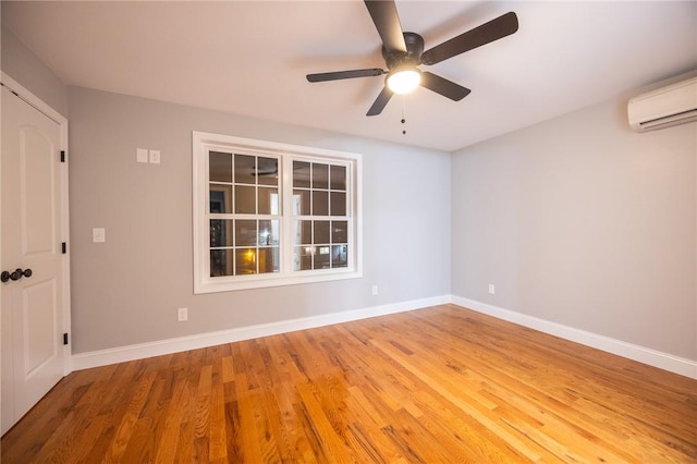 empty room with a wall mounted AC, wood-type flooring, and ceiling fan