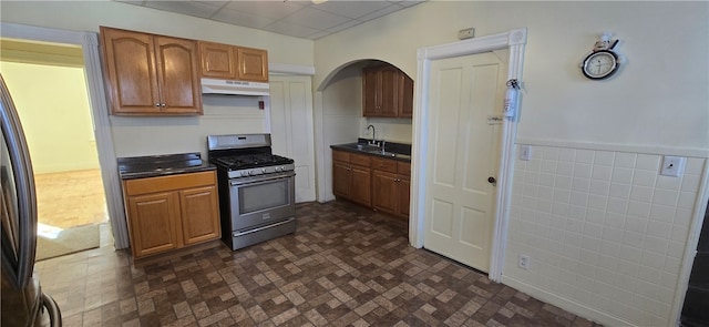 kitchen with a drop ceiling, stainless steel gas range oven, black fridge, and sink